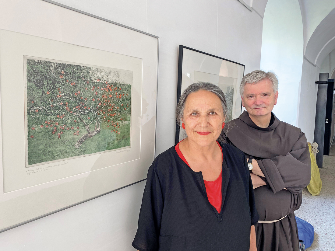 Die Künstlerin Hannelore Nenning kuratiert die Ausstellung im Franziskanerkloster. Hier steht sie neben ihrem Bild „Neues Leben im alten Apfelbäumchen“. P. Johannes Schneider OFM ist der Salzburger unter den Künstlern, deren Werke zu sehen sind.